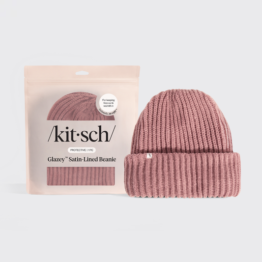 Pink beanie with satin lining next to its packaging on a light gray background